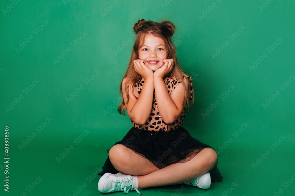 Teenage girl in colorful clothes on a green background with a charming smile. The child is sitting on the floor. Teenage girl in colorful clothes on a green background with a charming smile. The child is sitting on the floor.