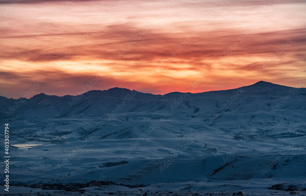 Beautiful winter landscape. The mountains peaks snow-covered on the sunset. Dramatic sky.