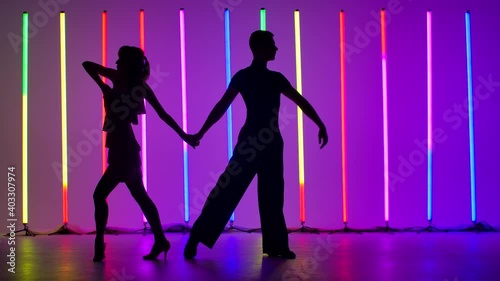 A couple of dancers are dancing a passionate Latin American dance. Rumba, samba, cha cha cha, jive. Dark silhouettes of dancers against the background of bright multicolored neon lamps. Slow motion.