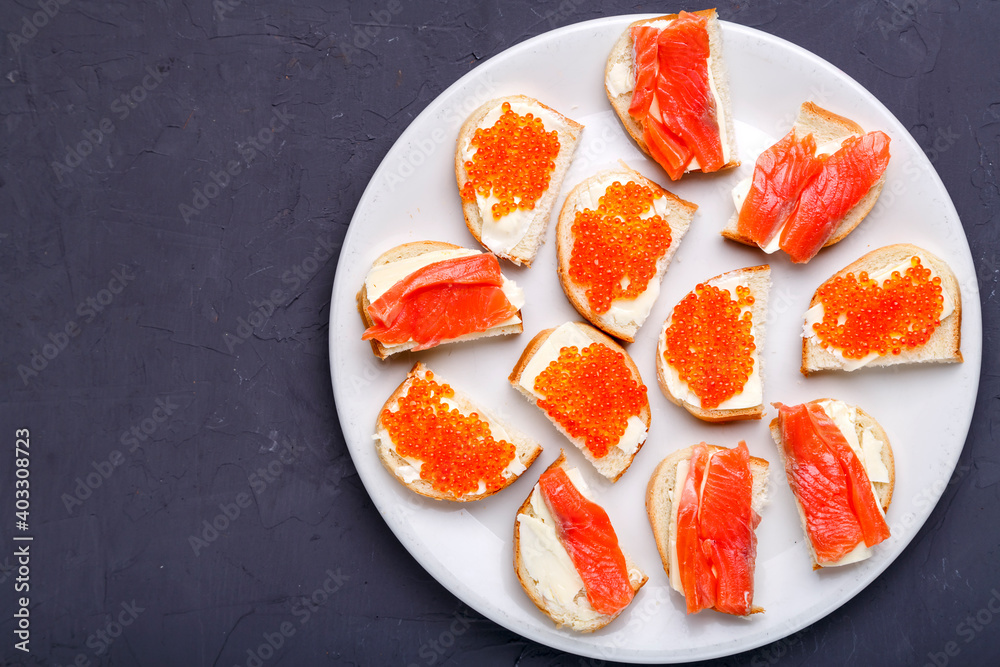 Bruschettes with butter and red caviar and salmon on a white plate on a gray concrete background copy space. Bruschettes with butter and red caviar and salmon on a white plate on a gray concrete background copy space.