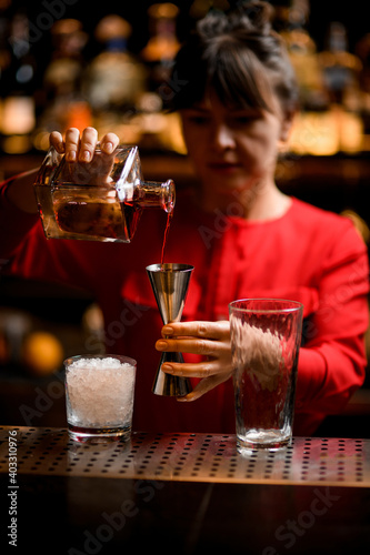 polished jigger in hand of female bartender in which she pours drink from bottle
