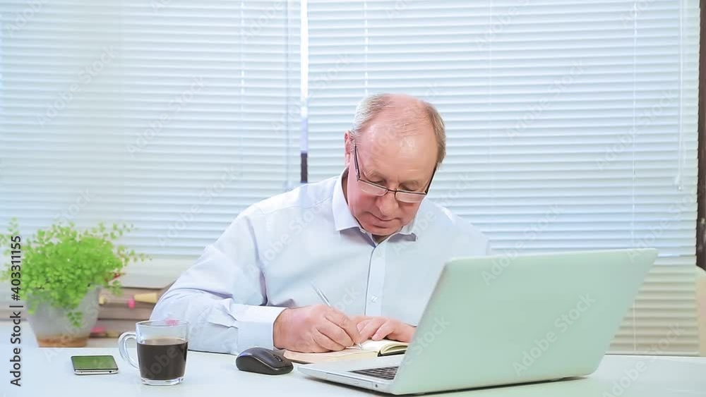 male leader with glasses in the office at the computer works and with projects. Medium plan male leader with glasses in the office at the computer works and with projects. Medium plan