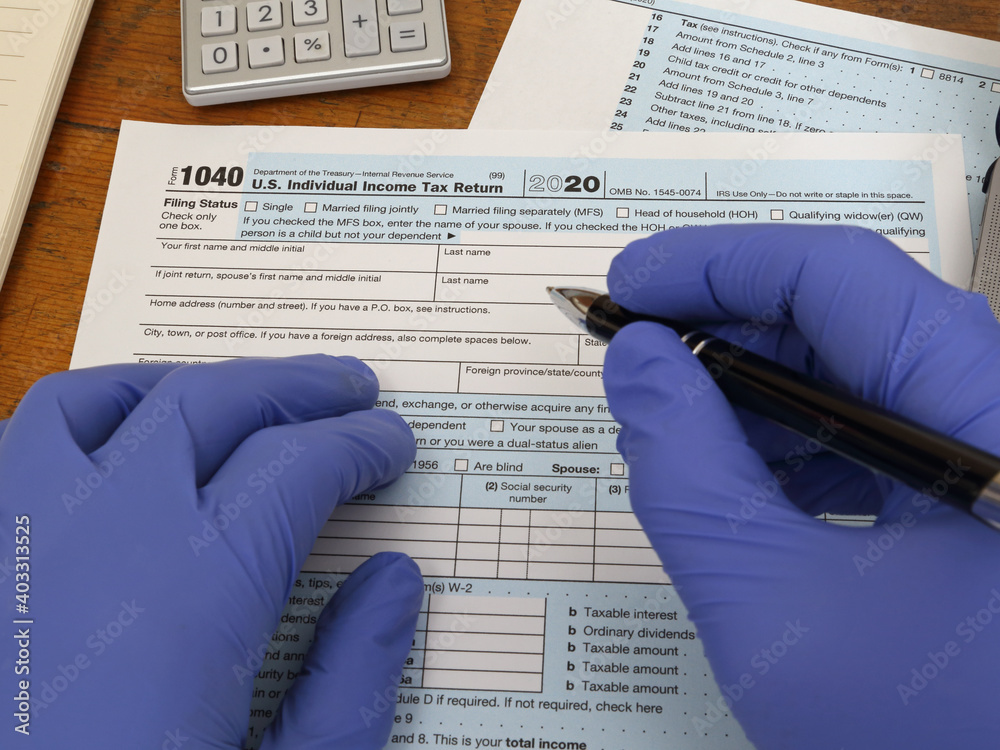 Hands wearing blue nitrile rubber gloves are shown starting to fill out a U.S. tax form 1040