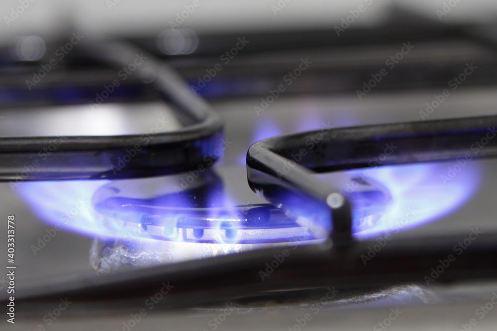 Stainless steel gas stove hob with blue fire close up, kitchen indoor