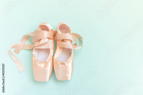 Fotografia New pastel beige ballet shoes with satin ribbon isolated on blue background