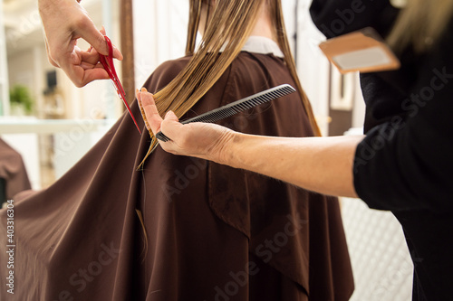 Closeup of hands of hairdresser cutting long blond hair in hair salon
