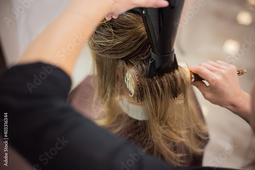 Closeup of hands of hairdresser while blowdrying hair of customer in the hair salon