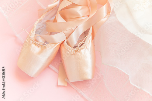 New pastel beige ballet shoes with satin ribbon and tutut skirt isolated on pink background. Ballerina classical pointe shoes for dance training. Ballet school concept. Top view flat lay, copy space