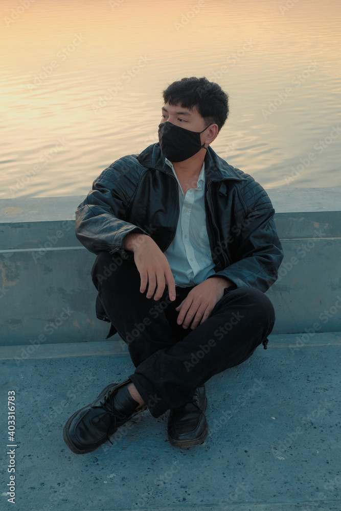 Asian man sit at riverside with black fabric face mask Asian man sit at riverside with black fabric face mask