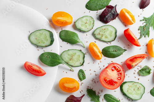 Flat layered fresh vegetables, herbs and spices with an empty white plate on a white background. Images of text space. Healthy Eating Concepts