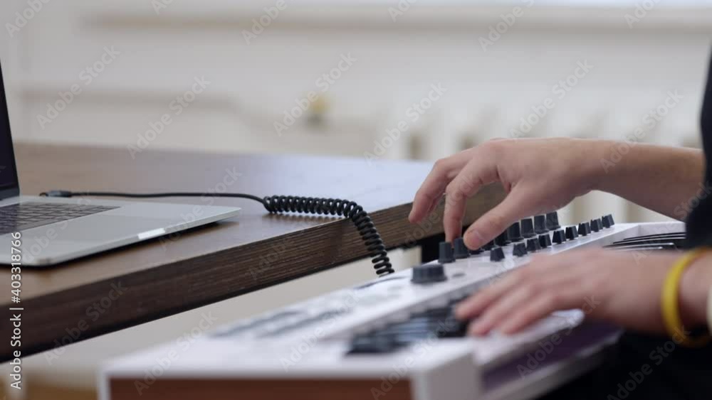 Close up of a guy musician plays on a midi keyboard connected to a laptop.