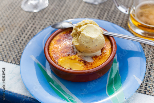 Closeup shot of a delicious dessert, creme brulee and ice cream, placed on top of a delicate and colorful plate, with beer placed on side, at Paris