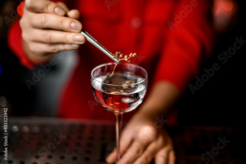 close-up on wineglass and woman's hand holding tweezers with plant above it