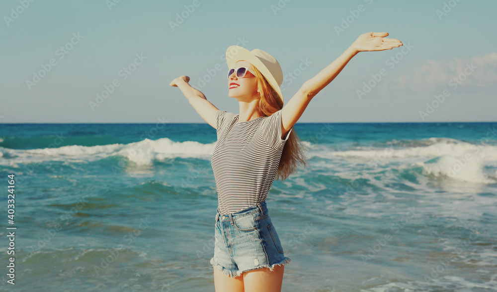 Happy smiling woman raising her hands up on the beach over sea background at summer day Happy smiling woman raising her hands up on the beach over sea background at summer day