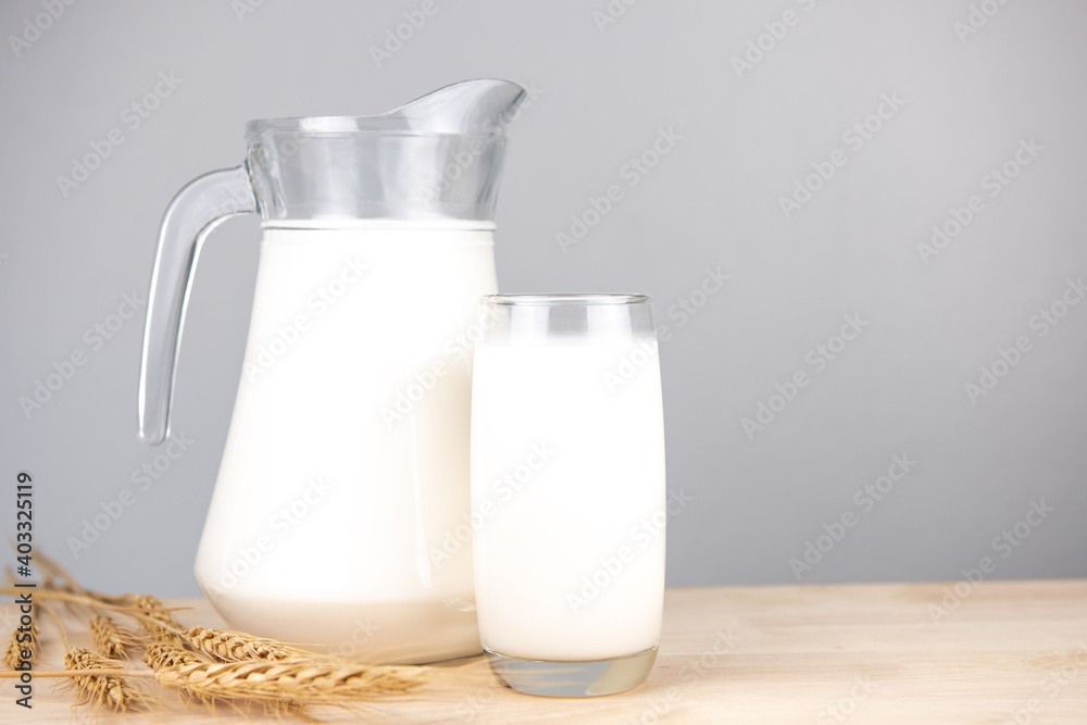 Jug of fresh milk glass on barley wheat and wooden background. Raw milk is high in calcium and protein to drink for all ages. Milk consumption nutritious and healthy dairy products concept. Jug of fresh milk glass on barley wheat and wooden background. Raw milk is high in calcium and protein to drink for all ages. Milk consumption nutritious and healthy dairy products concept.