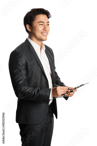 Attractive asian businessman in a dark grey suit holding a clipboard looking away from camera smiling. White background.
