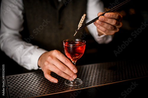 barman's hand holds glass of drink and decorates it with wheat spikelet