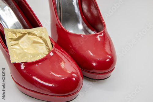 A classic sexy pair of red high heels stilettos with a gold condom wrapper on a white background
