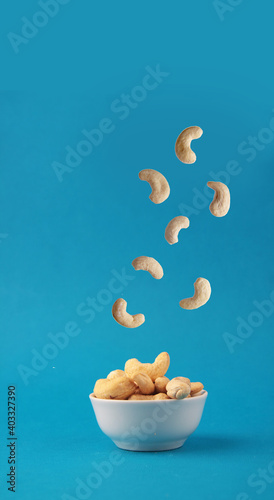cashew pouring into white bowl against blue background. Concept of flying food