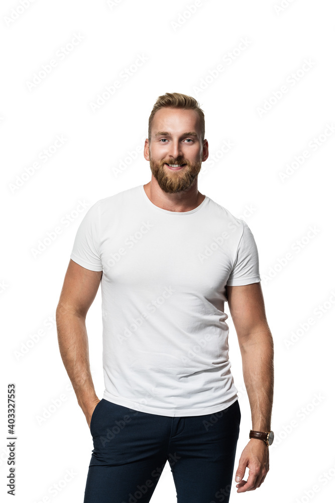 Relaxed attractive blonde bearded man standing against a white background wearing a white t-shirt, smiling towards camera. - obrazy, fototapety, plakaty 
