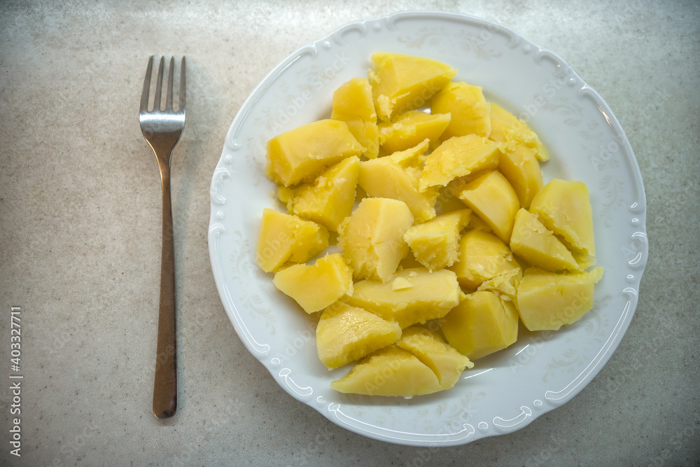 Boiled yellow potatoes on a white plate, next to a fork. Boiled yellow potatoes on a white plate, next to a fork.