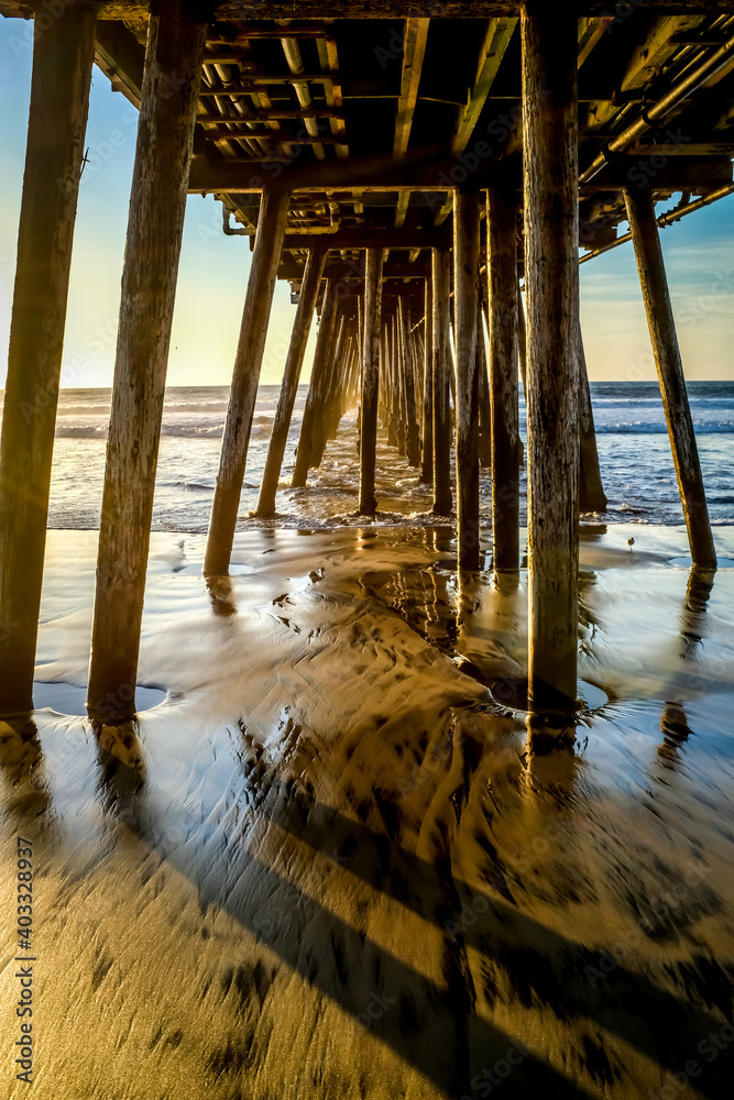 Pacific Ocean rising tide under pier with sand and reflection of water