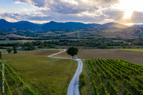 Aerial view of a winding road on the hills surrounding the town of Fabriano, in the Italian Marche region. A car is parked on a lonely road during a wonderful sunset.