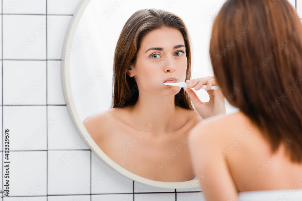 young woman brushing teeth near mirror in bathroom, blurred foreground young woman brushing teeth near mirror in bathroom, blurred foreground