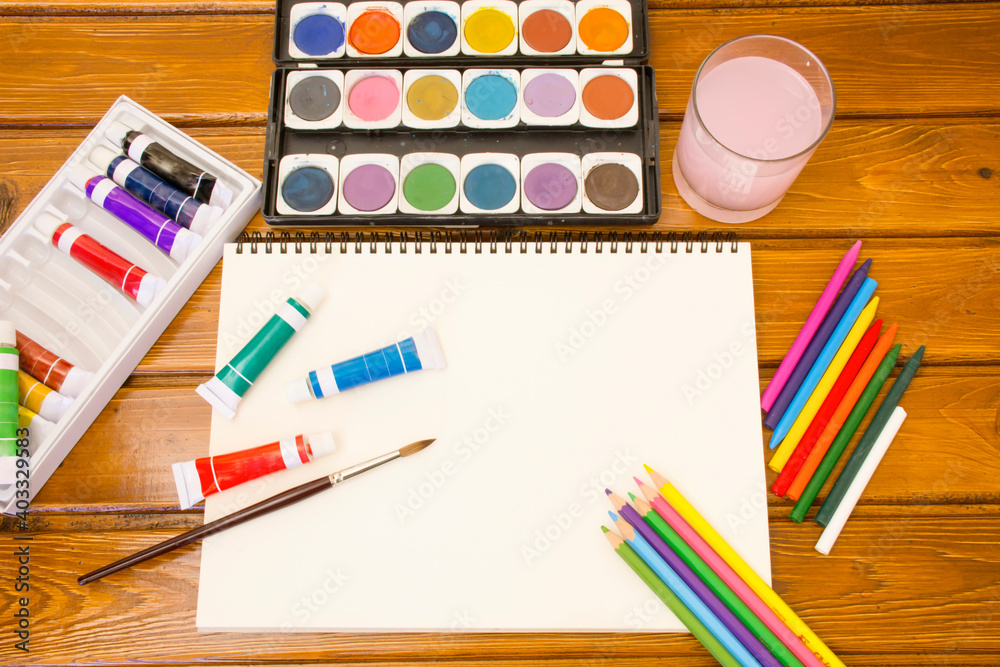 Naklejka premium Wooden background with set of color pencils used water color box, tube colors