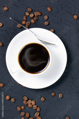 A white cup of hot coffee on black background. Flat lay. Coffee beans on a black table. Morning coffee