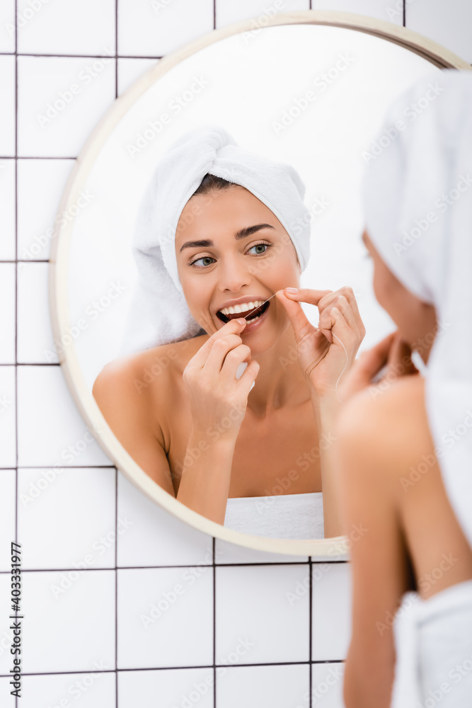 young woman with white towel on head flossing teeth near mirror in bathroom, blurred foreground young woman with white towel on head flossing teeth near mirror in bathroom, blurred foreground