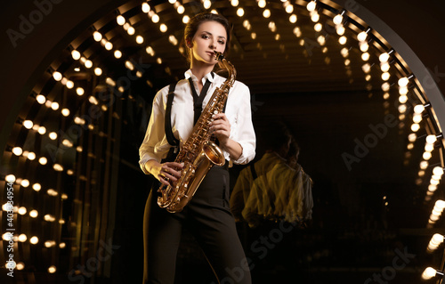 Gorgeous brunette model woman in fashionable formal suit with saxophone
