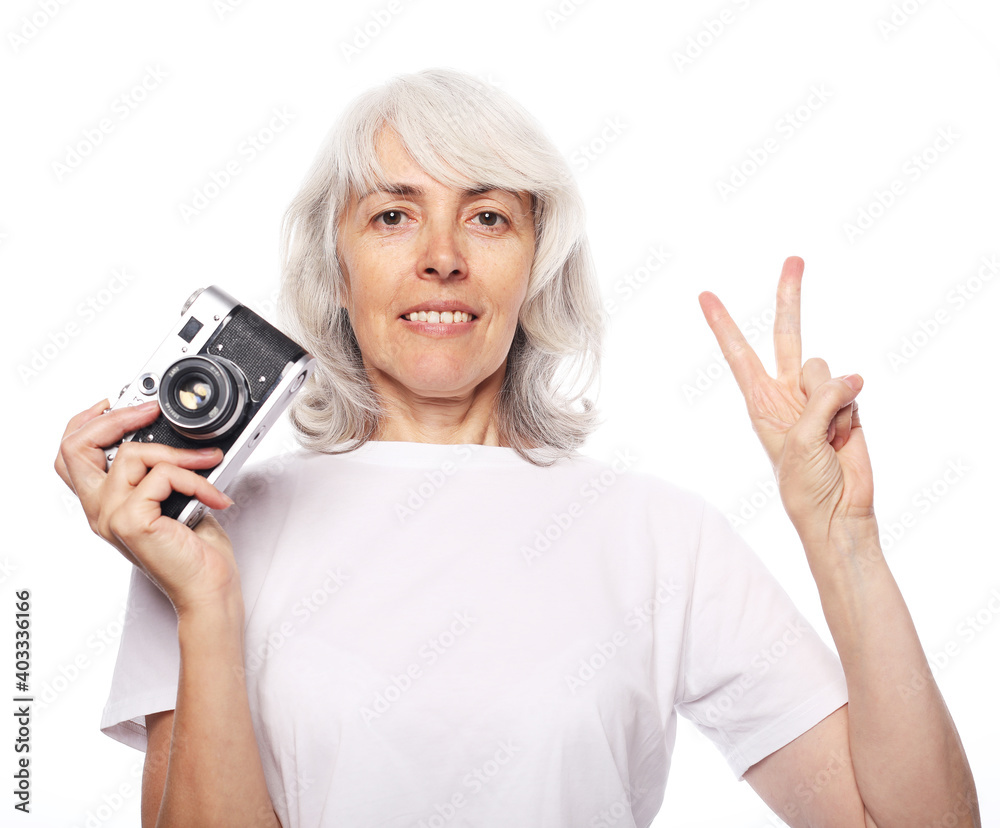 Lifestyle and people comcept: Happy elderly woman is holding a camera and smiling. Shows the sign of victory. Lifestyle and people comcept: Happy elderly woman is holding a camera and smiling. Shows the sign of victory.