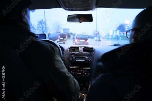two men are driving a car in the evening in the rain along city streets, the concept of road traffic, traffic jams, traveling by personal transport © kittyfly