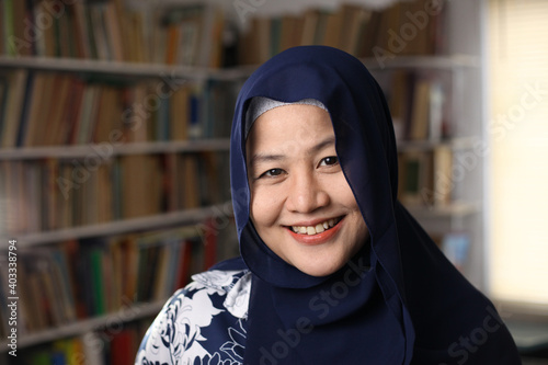 Happy beautiful Asian muslim woman wearing hijab smiling to camera, female student in library