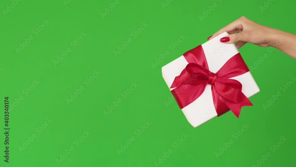 Holiday surprise. Women day present. Gift delivery. Special day congratulation. Female hand showing white wrapped box with red ribbon bow isolated on green empty space background loop. Holiday surprise. Women day present. Gift delivery. Special day congratulation. Female hand showing white wrapped box with red ribbon bow isolated on green empty space background loop.