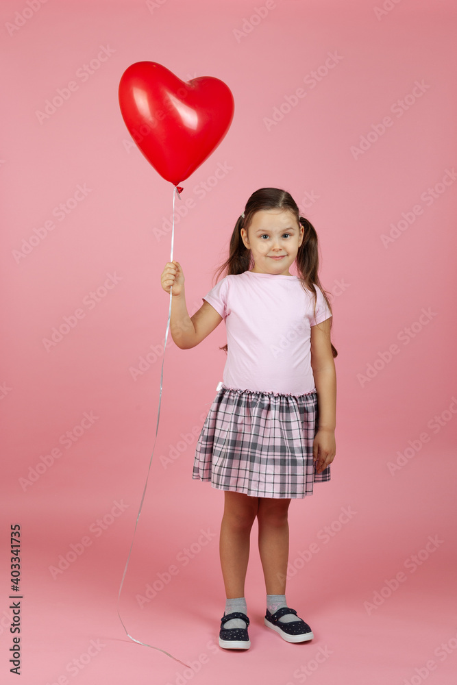 full-length smiling contented child in pink dress with red heart shaped balloon in hand isolated on pink background. full-length smiling contented child in pink dress with red heart shaped balloon in hand isolated on pink background.