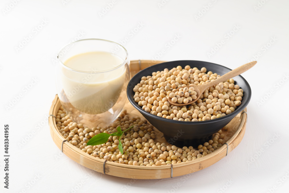 Soybeans seed in a black bowl with spoon and soy milk in a glass on bamboo tray with white background Soybeans seed in a black bowl with spoon and soy milk in a glass on bamboo tray with white background