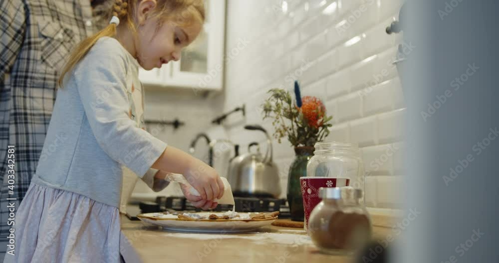 Young family spending time at home together. Mother and daughter having fun baking cooking christmas cookies pastry in the kitchen. Cute kid decorating biscuits with glaze. Young family spending time at home together. Mother and daughter having fun baking cooking christmas cookies pastry in the kitchen. Cute kid decorating biscuits with glaze.