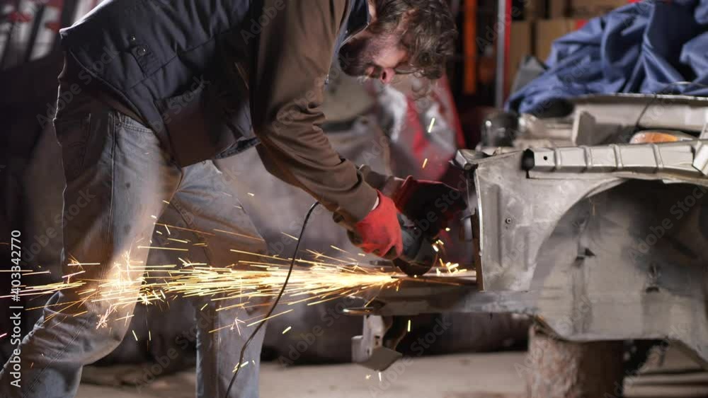 Mechanic man uses sparking circular saw on metal bodywork of car in workshop