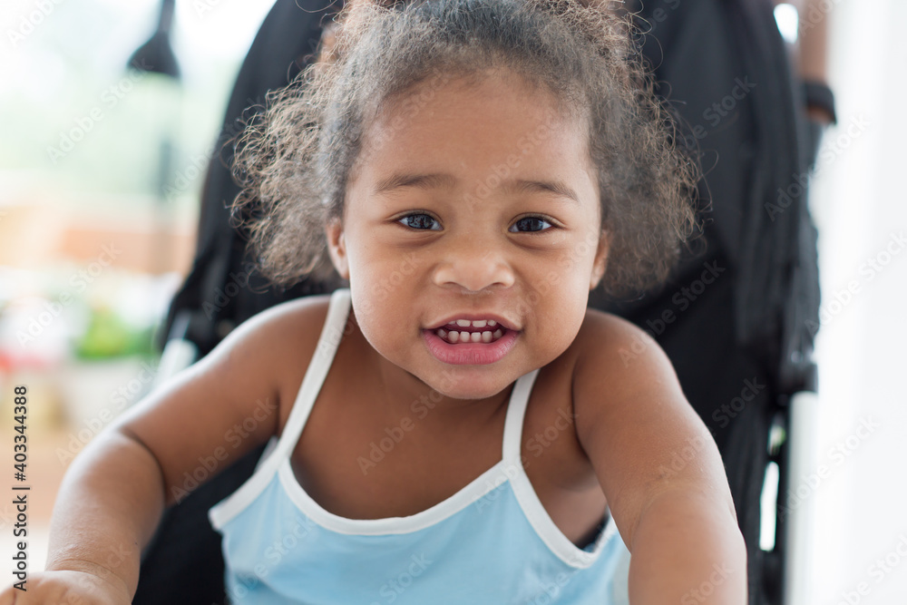 African American little girl with curly hair sitting and playing on stroller. Cheerful Afro toddler little girl sitting on stroller. Toddler child little girl enjoy, having fun at home African American little girl with curly hair sitting and playing on stroller. Cheerful Afro toddler little girl sitting on stroller. Toddler child little girl enjoy, having fun at home