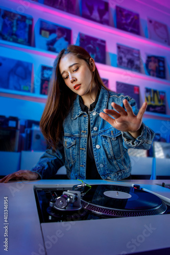 chica dj alegre mezclando pistas con discos de vinilo usando un tornamesa y una mezcladora en una tienda de discos.