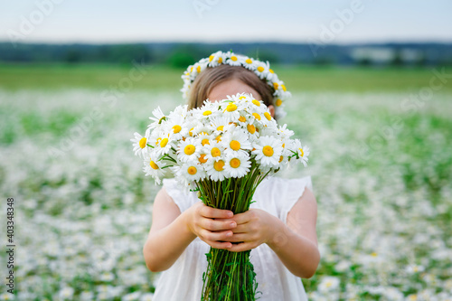 Selective focus. Cute girl with a bouquet of chamomile flowers and a wreath of daisies on her head in a field, holding a bouquet in front of her.