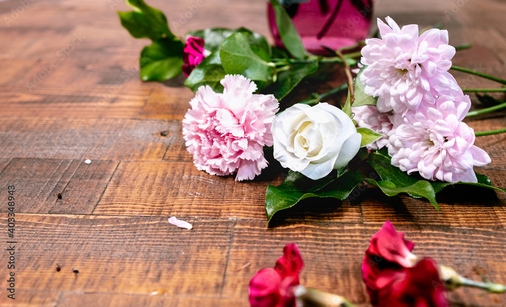Closeup front view of blossom flowers with fresh green leaves lay on a wooden table surface. Arranging white rose and pink florals for decoration on a special day. Happy romantic love concept.