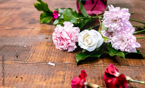 Closeup front view of blossom flowers with fresh green leaves lay on a wooden table surface. Arranging white rose and pink florals for decoration on a special day. Happy romantic love concept. © Vipada