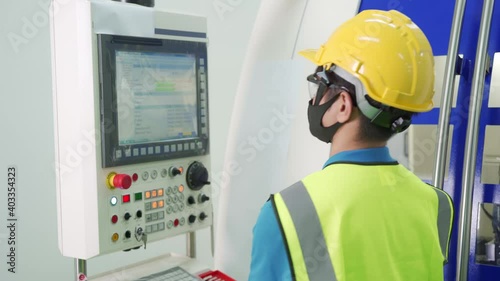 Asian production line operator in uniform and face mask work at control panel of CNC machine in factory. New normal working concept to prevent spread of Covid-19 Coronavirus