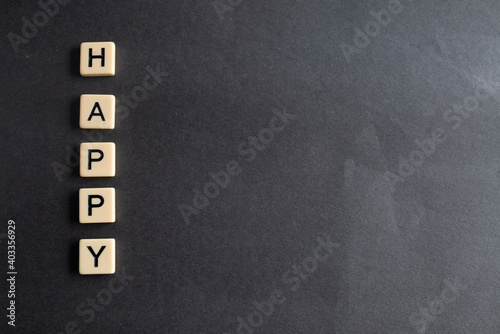 the words happy written as a flat lay in wood scrabble tiles on a plain black background