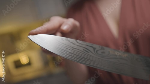 Close-up of woman holding sharp knife. Action. Woman checks sharpness of knife at tip before slicing. Woman intimidatingly holds knife before cooking in kitchen photo