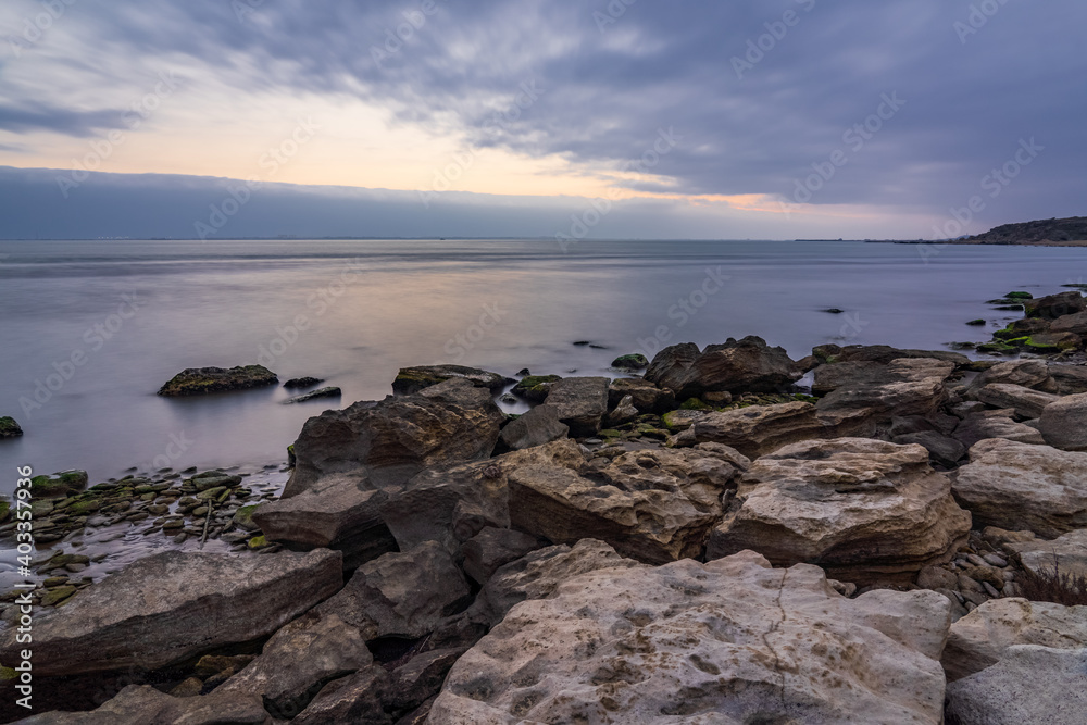 Cloudy sunrise on rocky sea coast, long exposure