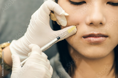Selection focus on syringe injection to face. Doctor cosmetologist makes the Rejuvenating facial injections procedure for tightening and smooth wrinkles on beautiful face skin. Add noise film grain.
